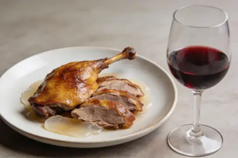 Un plat de canard rôti tranché, nappé de sauce, avec un verre de vin rouge. La question est : quel vin avec le canard ?
