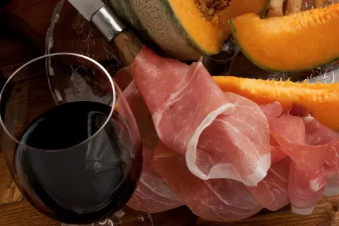 Un verre de vin rouge, du melon et du jambon cru. Quel vin avec melon et jambon cru ? Une belle association pour un apéritif gourmand.