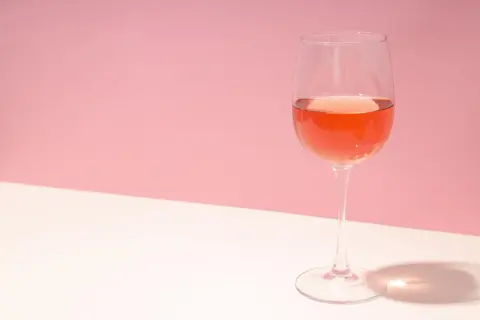 Verre de rosé très clair sur fond rose et blanc, avec une ombre projetée.