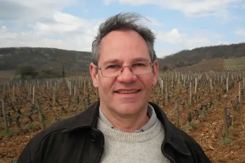 Alain Gras, souriant, se tient devant un vignoble vallonné.