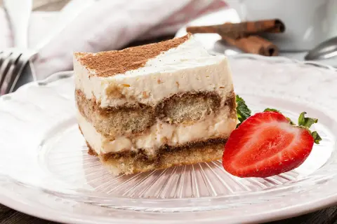 Tranche de tiramisu sans oeuf, garnie de cacao et d'une fraise fraîche, sur une assiette rose.