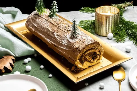 Une délicieuse recette de buche de Noel au chocolat, décorée de sapins miniatures et de neige, prête à être dégustée.