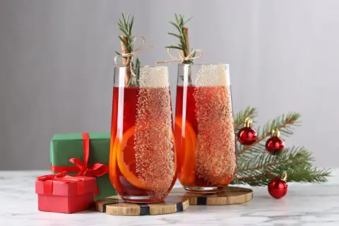 Deux verres de cocktail de Noël facile et rapide, décorés d'orange et de cannelle, avec des cadeaux et un sapin en arrière-plan.