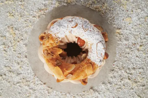 Un Paris-Brest aérien, garni d'une crème onctueuse au praliné noisette, saupoudré de sucre glace et d'amandes effilées.