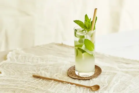 Un verre de nom de cocktail rafraîchissant avec de la menthe et de la glace, sur une nappe en dentelle.