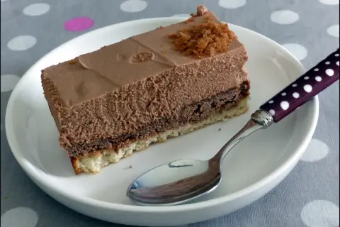 Une part de **Trianon gâteau** au chocolat, légère et aérienne, sur une assiette blanche avec une cuillère à pois.