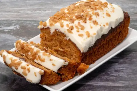 Un délicieux gâteau carotte, généreusement glacé et parsemé de noix croquantes, est servi sur une assiette blanche.