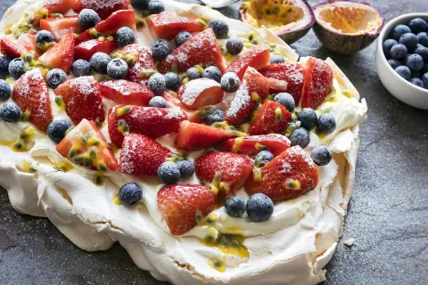 Pavlova recette : meringue aérienne garnie de crème fouettée, fraises, myrtilles et fruits de la passion. Un délice !