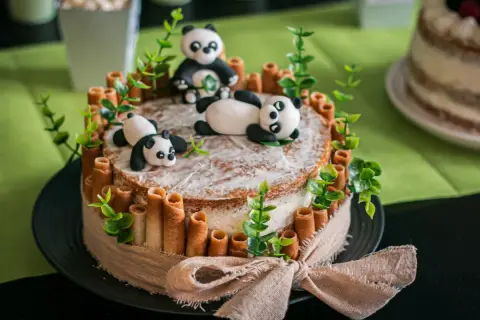Un adorable layer cake anniversaire facile avec des pandas en pâte à sucre, des rouleaux de biscuit et des feuilles vertes.