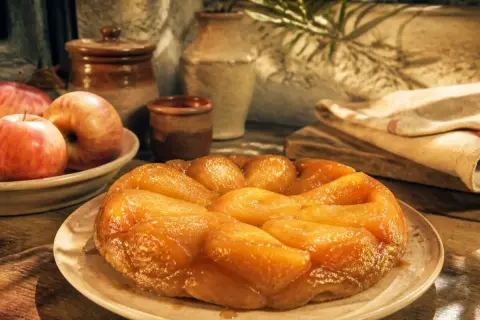 Une tarte tatin inratable, dorée et caramélisée, prête à être dégustée. Des pommes fraîches l'accompagnent.