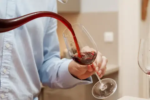 Un homme verse du vin rouge d'un **decanter ou carafer** dans un verre. Une autre bouteille et un verre vide sont visibles.