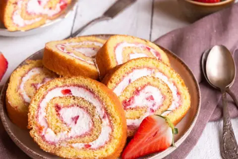 Tranches de gâteau roulé aux fraises et à la crème, parfaites pour une recette gâteau roulé facile. Une fraise coupée est posée sur l'assiette.