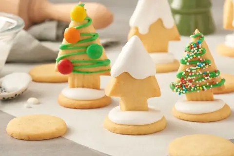 Biscuits en forme de sapins décorés de glaçage vert, vermicelles colorés et bonbons. Une recette festive à partager.