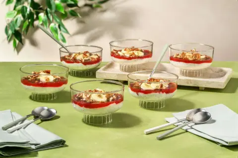 Six coupes de dessert aux graines de chia, garnies de compote de fraises, de rondelles de banane et de noix, parfaites pour un goûter.