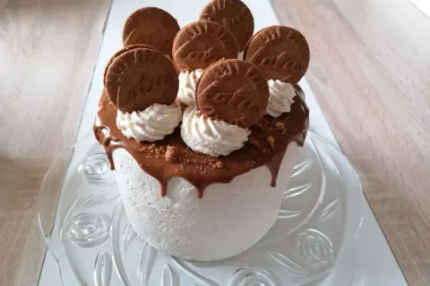 Gâteau blanc crémeux, nappé de chocolat fondant et décoré de biscuits spéculoos et de crème fouettée.