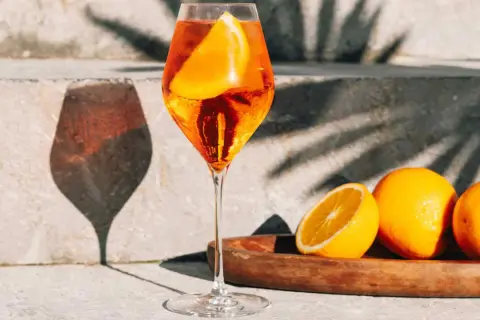 Un verre de Spritz pétillant, garni d'une tranche d'orange, avec des oranges fraîches sur un plateau. Parfait pour une recette spritz d'été.