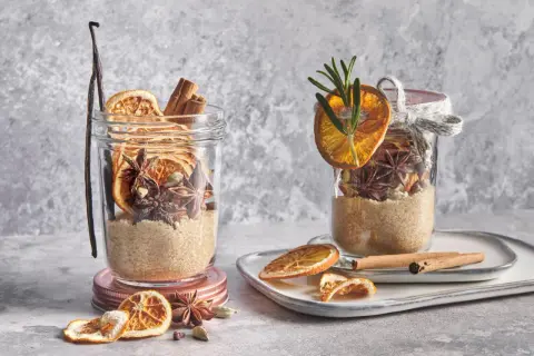 Ingrédients pour une recette de vin chaud : sucre, bâtons de cannelle, anis étoilé, cardamome, orange séchée et vanille dans des bocaux.
