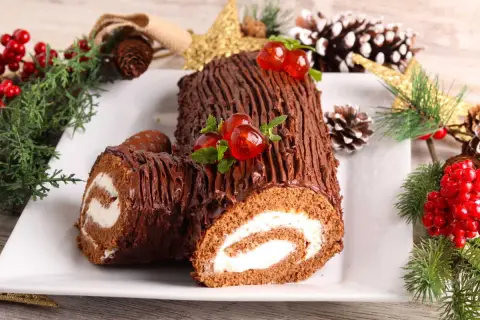 Un délicieux biscuit roulé moelleux au chocolat, décoré de cerises et de menthe, entouré de décorations de Noël.