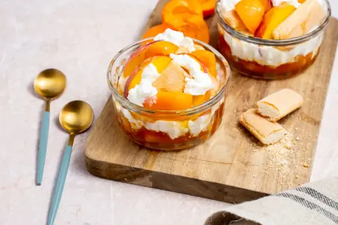 Délicieux dessert printemps : couches de fruits d'abricot, de biscuits à la cuillère et de crème fouettée dans des coupes en verre.