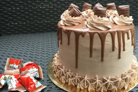 Gâteau au chocolat avec ganache Kinder Bueno, décoré de rosettes et de morceaux de chocolat.