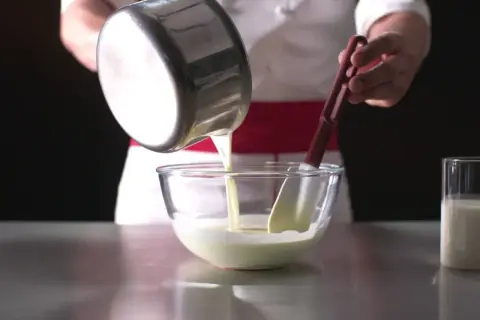 Un chef verse un liquide crémeux dans un bol, préparant une délicieuse namelaka vanille.