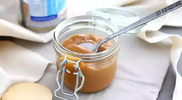 Un pot de confiture de lait onctueuse, une cuillère décorée et des biscuits sablés, prêts à être dégustés.