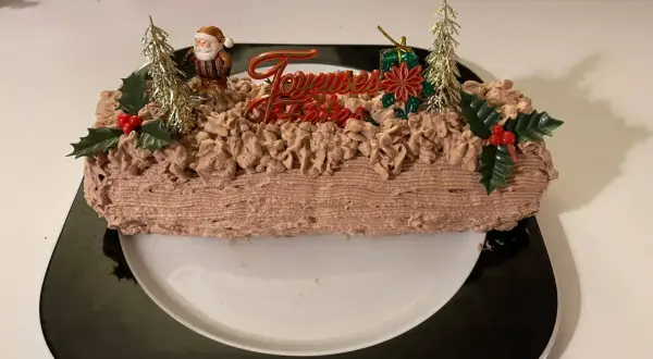 Bûche de Noël au chocolat, décorée de chantilly mascarpone, d'un Père Noël et de sapins dorés.