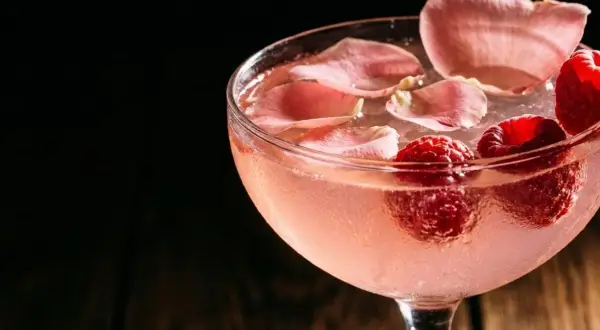 Cocktail rosé rafraîchissant garni de framboises et de pétales de rose. Une recette délicieuse pour l'été.