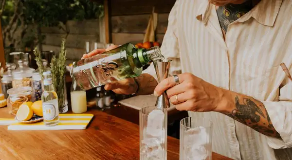 Un barman prépare un cocktail, versant du gin alcool de quoi dans un verre rempli de glaçons.