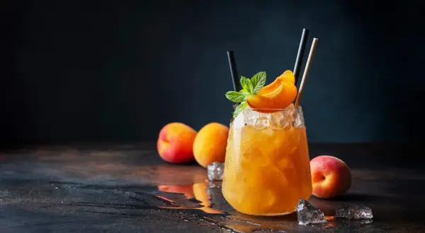 Un cocktail rafraîchissant au jus d'abricot alcool, garni d'une tranche d'abricot et de menthe, sur un lit de glace pilée.