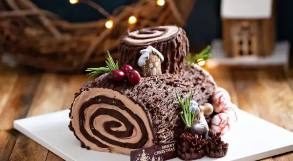 Bûche de Noël chocolatée, parfaite pour une recette génoise bûche moelleuse. Décorée de baies, romarin et d'une mini maison.