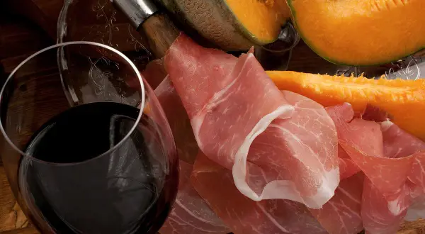 Un verre de vin rouge, du melon et du jambon cru. Quel vin avec melon et jambon cru ? Une belle association pour un apéritif gourmand.