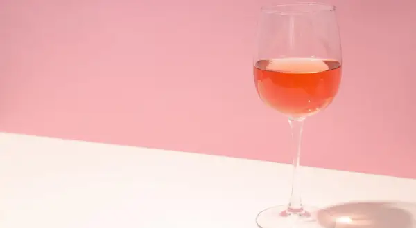 Verre de rosé très clair sur fond rose et blanc, avec une ombre projetée.