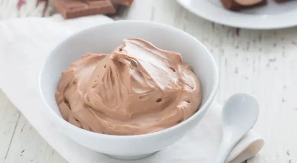 Un bol de namelaka chocolat onctueux, prêt à être dégusté. Des morceaux de chocolat sont visibles en arrière-plan.