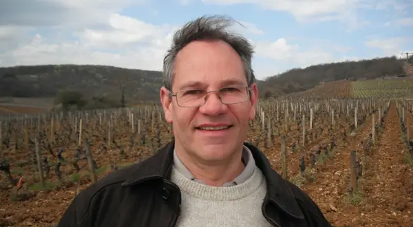Alain Gras, souriant, se tient devant un vignoble vallonné.