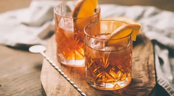Deux verres d'armagnac digestif ambré, glacés et garnis d'une tranche d'orange, sur une planche en bois.