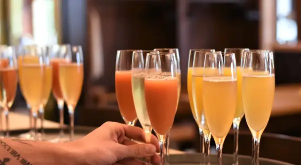 Une main saisit un verre de cocktail avec champagne, prêt à être servi. Plusieurs autres verres pétillants sont alignés.