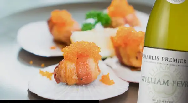 Coquilles Saint-Jacques garnies de caviar orange, accompagnées d'une bouteille de Chablis. Quel vin avec coquille saint jacques ? Un accord parfait.