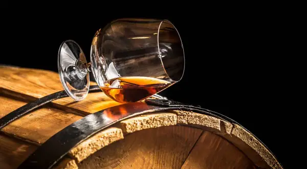 Verre de cognac renversé sur un tonneau en bois. Le liquide ambré suggère une question : le vin est-il un spiritueux ?