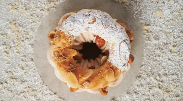 Un Paris-Brest aérien, garni d'une crème onctueuse au praliné noisette, saupoudré de sucre glace et d'amandes effilées.