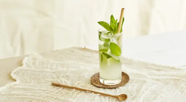 Un verre de nom de cocktail rafraîchissant avec de la menthe et de la glace, sur une nappe en dentelle.