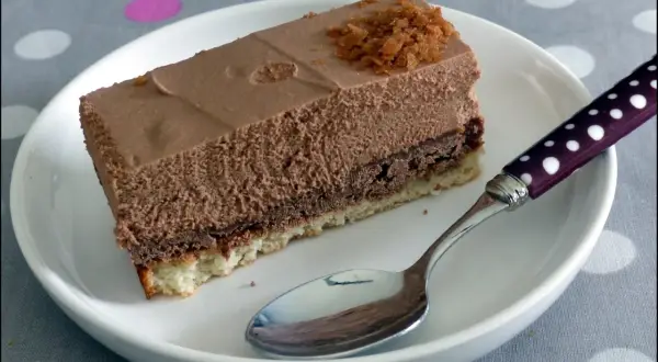 Une part de **Trianon gâteau** au chocolat, légère et aérienne, sur une assiette blanche avec une cuillère à pois.