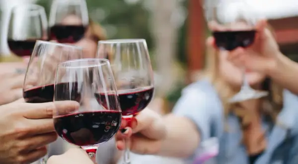 Des mains lèvent des verres de vin rouge pour un apéritif convivial.