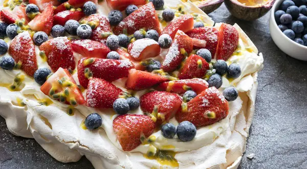 Pavlova recette : meringue aérienne garnie de crème fouettée, fraises, myrtilles et fruits de la passion. Un délice !