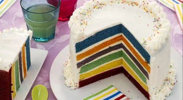 Un gâteau arc en ciel aux couches colorées, décoré de crème et de vermicelles, prêt à être dégusté.