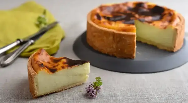 Un flan pâtissier onctueux sur une pâte feuilletée ou brisée dorée, avec une part coupée. Un délice à déguster !