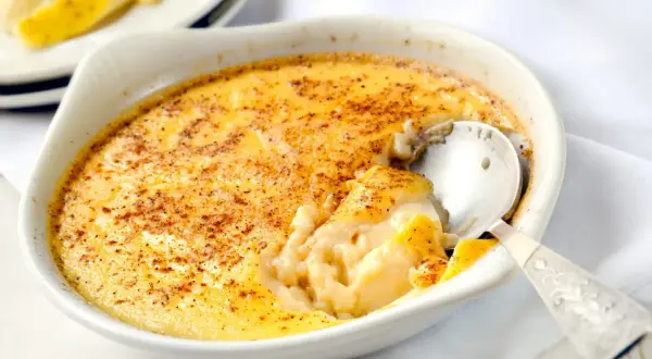 Un délicieux oeuf au lait crémeux, saupoudré de cannelle, est servi dans un ramequin blanc. Une cuillère en argent est enfoncée dans le dessert.