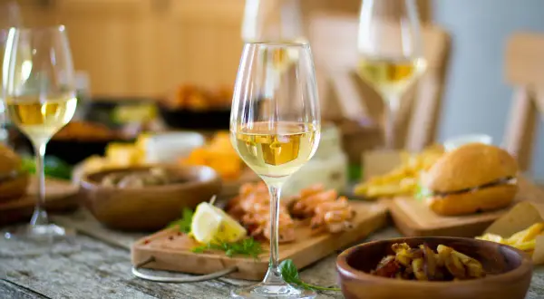 Verre de bordeaux blanc moelleux, parfait accompagnement pour crevettes, frites et mini-burgers sur une table rustique.