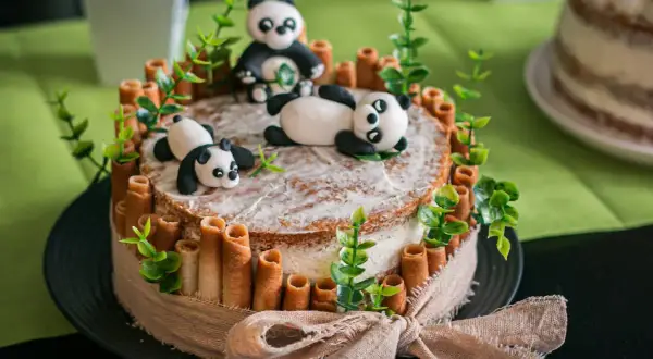 Un adorable layer cake anniversaire facile avec des pandas en pâte à sucre, des rouleaux de biscuit et des feuilles vertes.