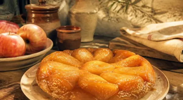 Une tarte tatin inratable, dorée et caramélisée, prête à être dégustée. Des pommes fraîches l'accompagnent.